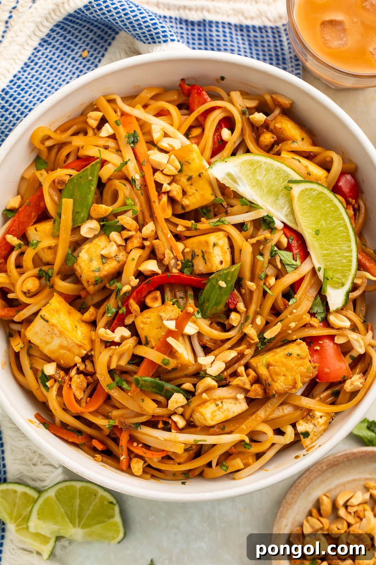 A beautifully arranged bowl of vegan pad thai on a wooden table, accompanied by a blue kitchen towel.