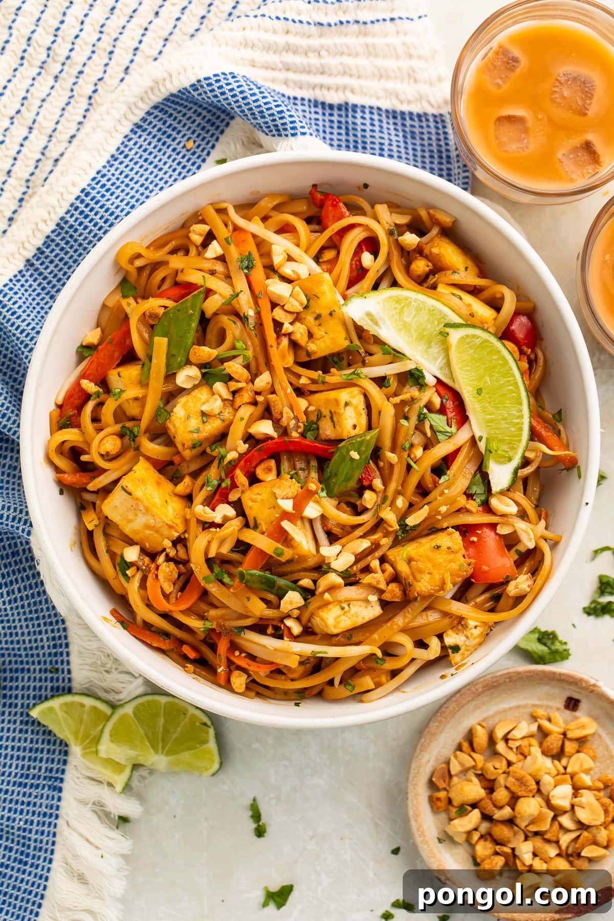 A beautifully plated bowl of vegan pad thai, garnished with peanuts and lime, on a rustic table.