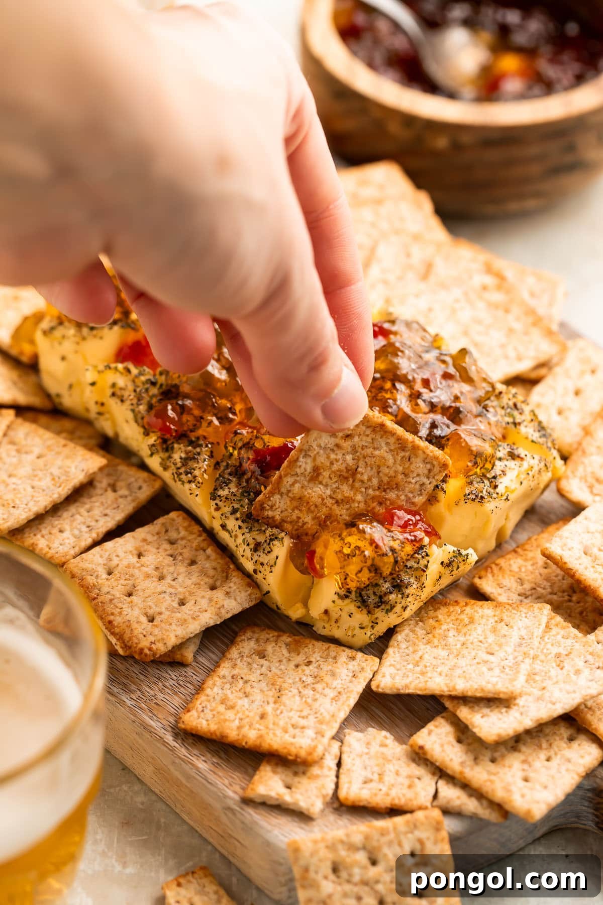A woman's hand scoops a generous portion of smoked cream cheese with a square wheat cracker, highlighting its smooth, spreadable texture.
