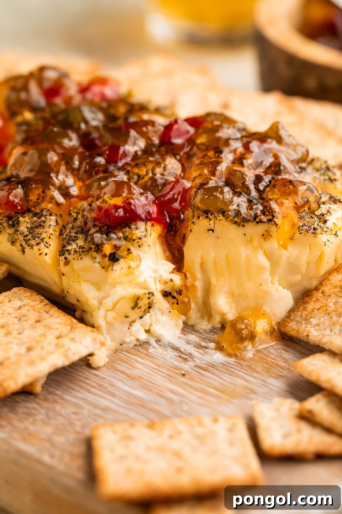 A block of smoked cream cheese, artfully topped with vibrant red pepper jelly, with a corner scooped out to reveal the creamy interior.