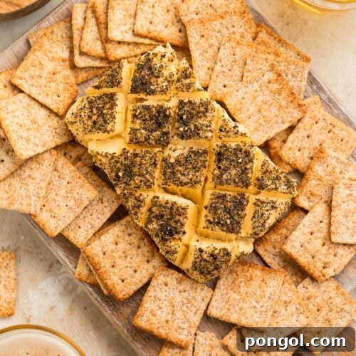 A block of smoked cream cheese, seasoned and crosshatched, surrounded by square wheat crackers on a serving platter.