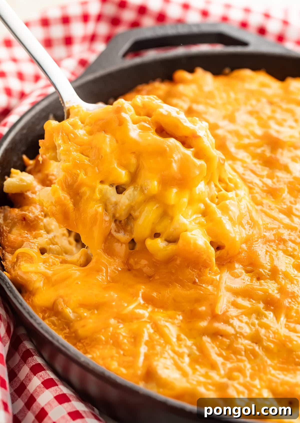 Creamy smoked mac and cheese in a cast iron skillet with a spoon lifting a portion showing the melted cheese texture