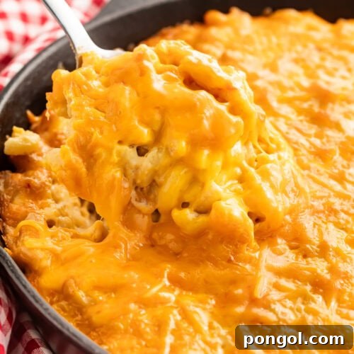 Creamy smoked mac and cheese in a cast iron skillet with a spoon lifting a portion showing the melted cheese texture