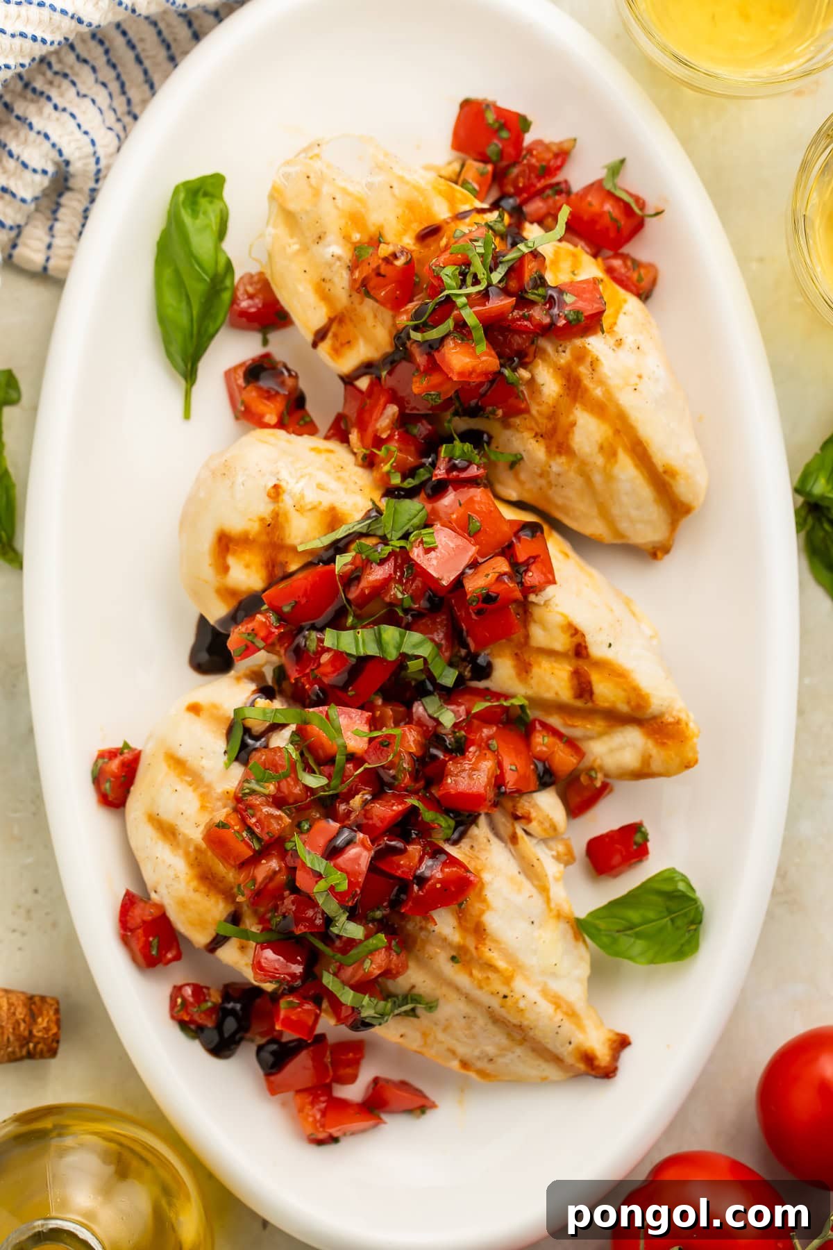 White oval serving dish of chicken breasts topped with chopped tomatoes, balsamic vinegar and fresh basil.