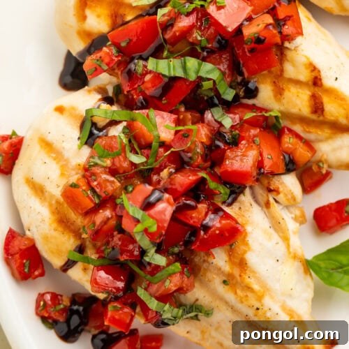 Close up of chicken breasts with bruschetta topping spooned over the top on a white plate.