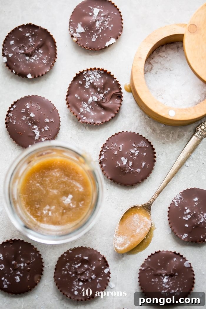Two rows of paleo chocolate cups with caramel, one bitten, showing the perfect layers of chocolate and gooey caramel inside, against a textured background.