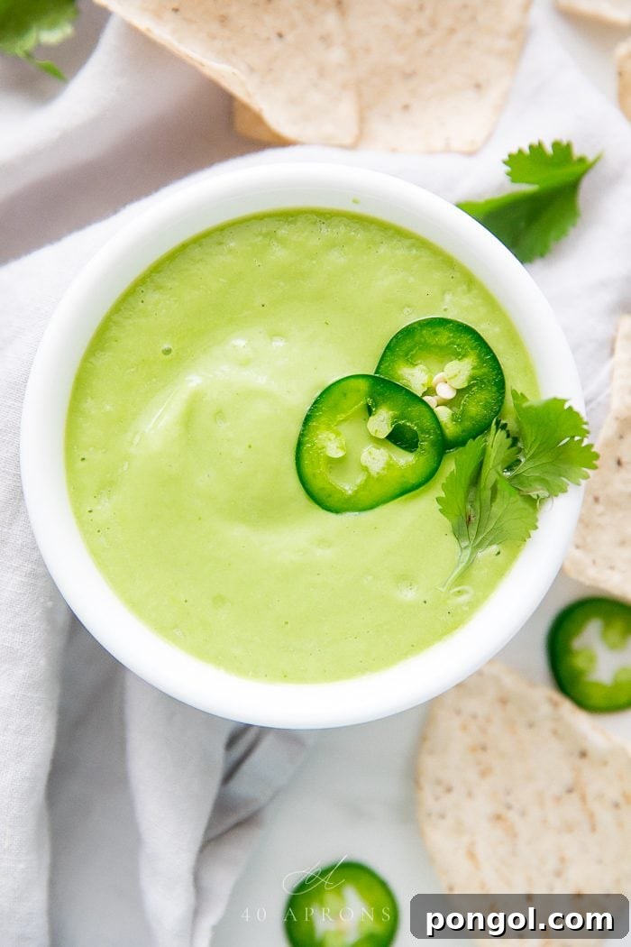 Smooth green avocado salsa in white bowl topped with jalapeño slices and cilantro