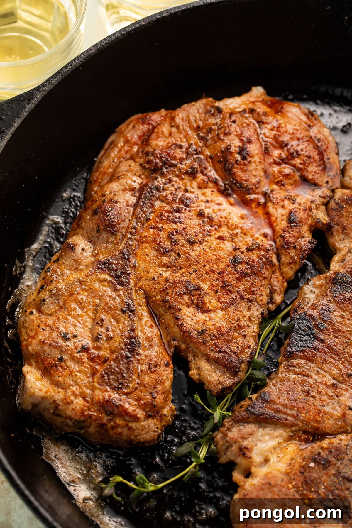 Golden-brown seared pork steaks in black cast iron skillet with fresh thyme sprigs
