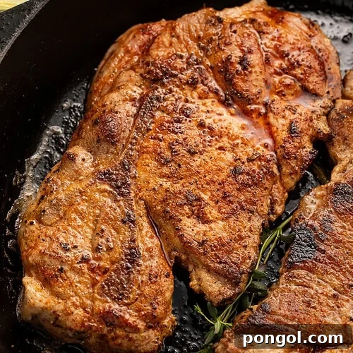 Golden-brown seared pork steaks in black cast iron skillet with fresh thyme sprigs