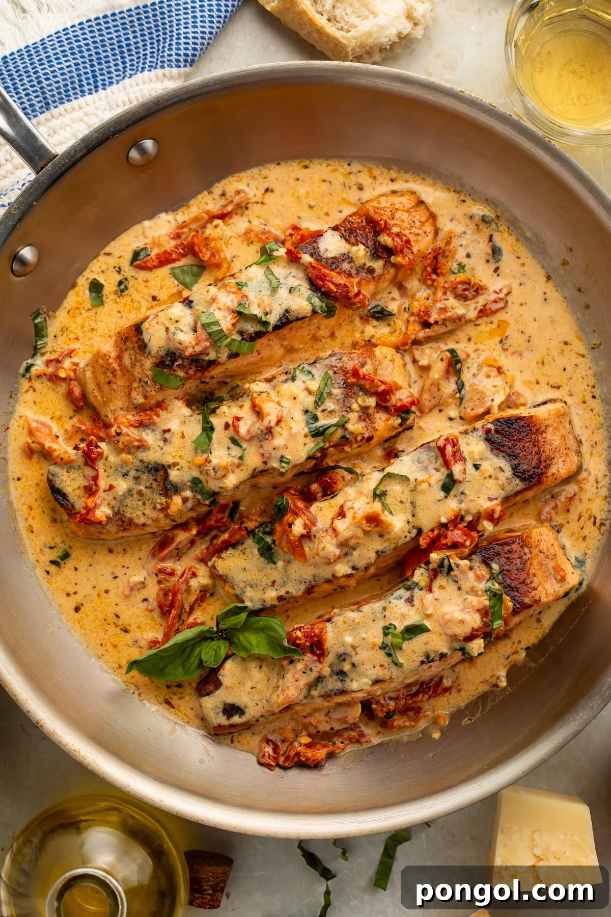 Pan-seared salmon with creamy parmesan sauce and sun-dried tomatoes in a stainless steel skillet, garnished with fresh basil.