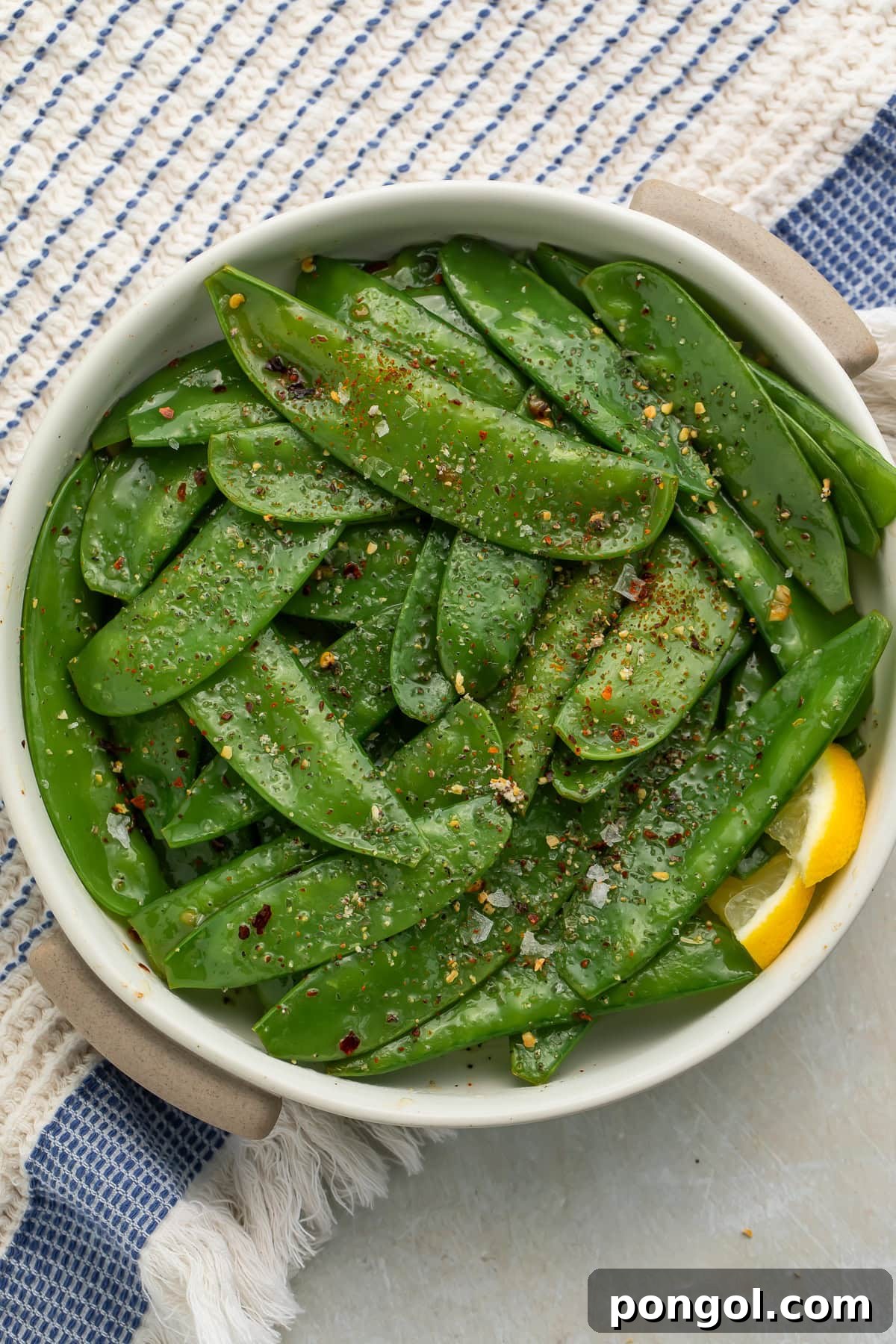 Garlic butter snow peas served in ceramic bowl with lemon wedge on striped kitchen towel