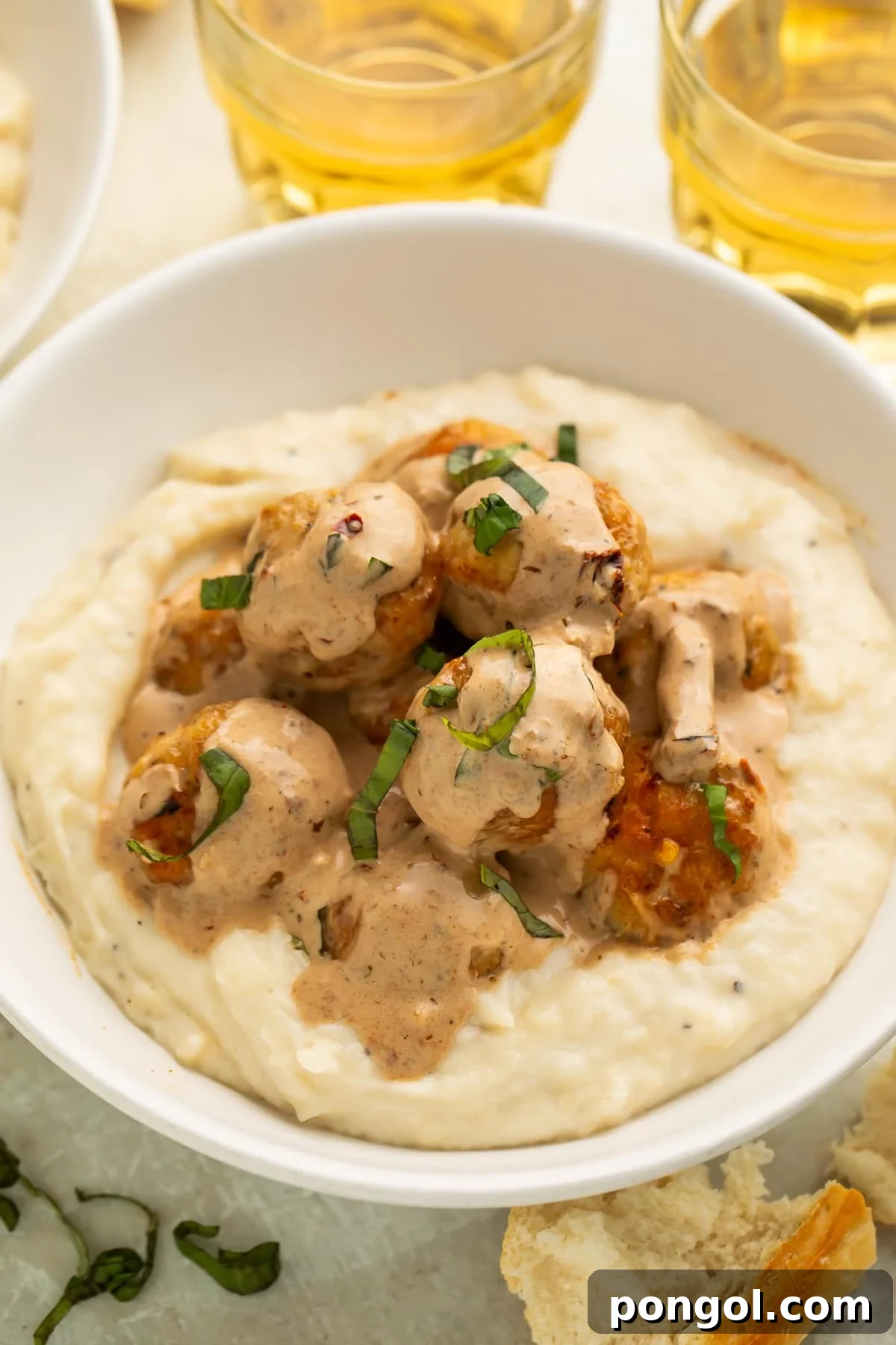 Marry me chicken meatballs served over creamy mashed potatoes in white bowls with wine glasses