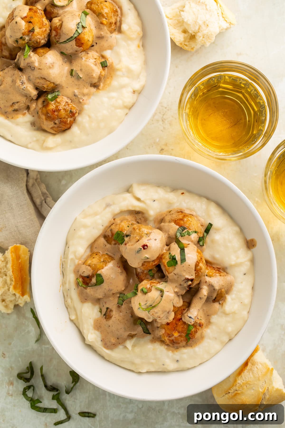Marry me chicken meatballs served over creamy mashed potatoes in white bowls with wine glasses