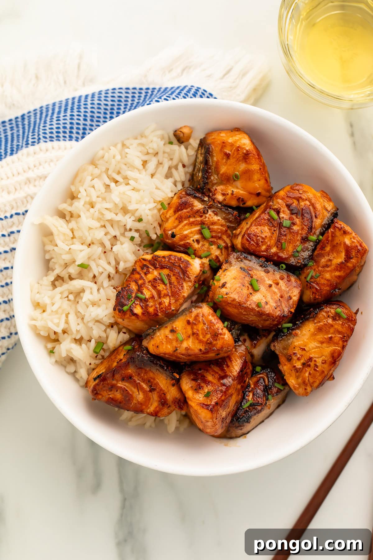Hot honey salmon bites and rice in white bowl with glass of white wine