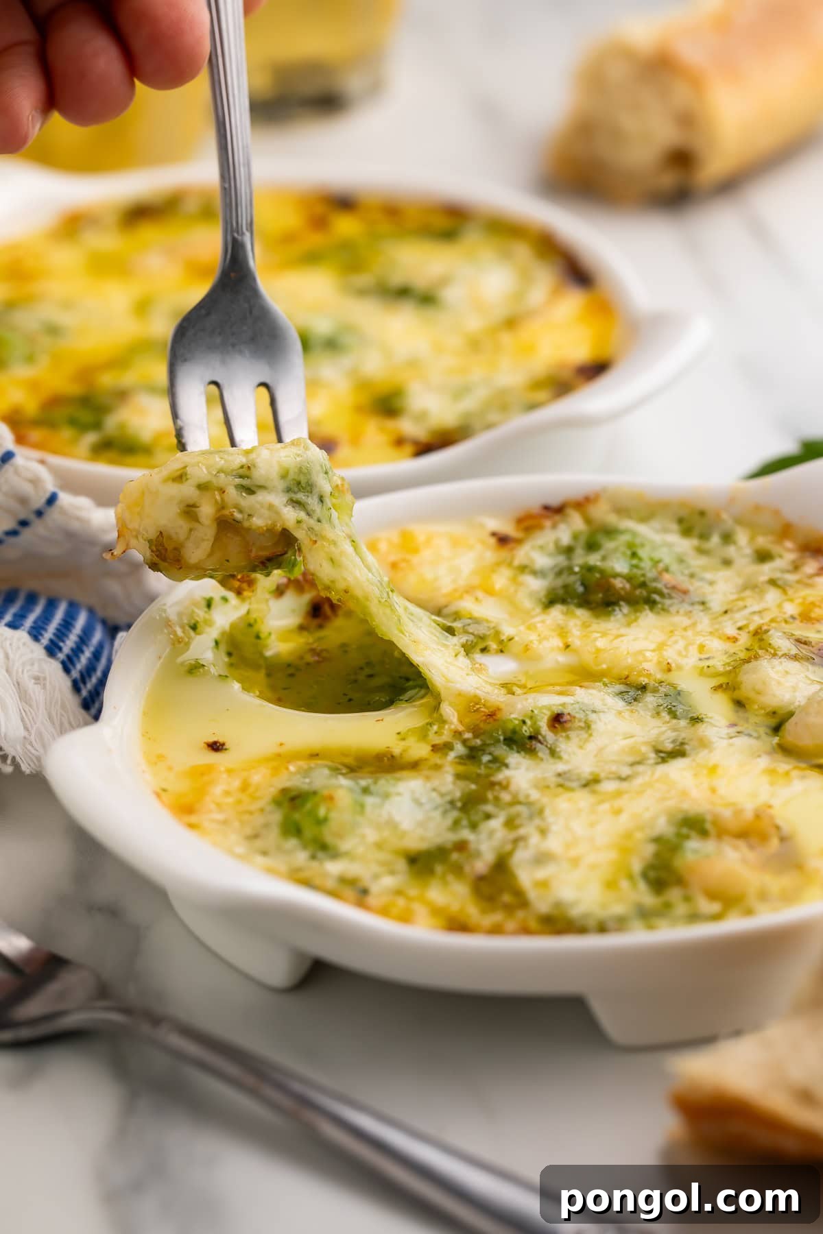A fork lifting a piece of lobster escargot, showing gooey melted cheese stretching from the ramekin, highlighting its delicious texture.