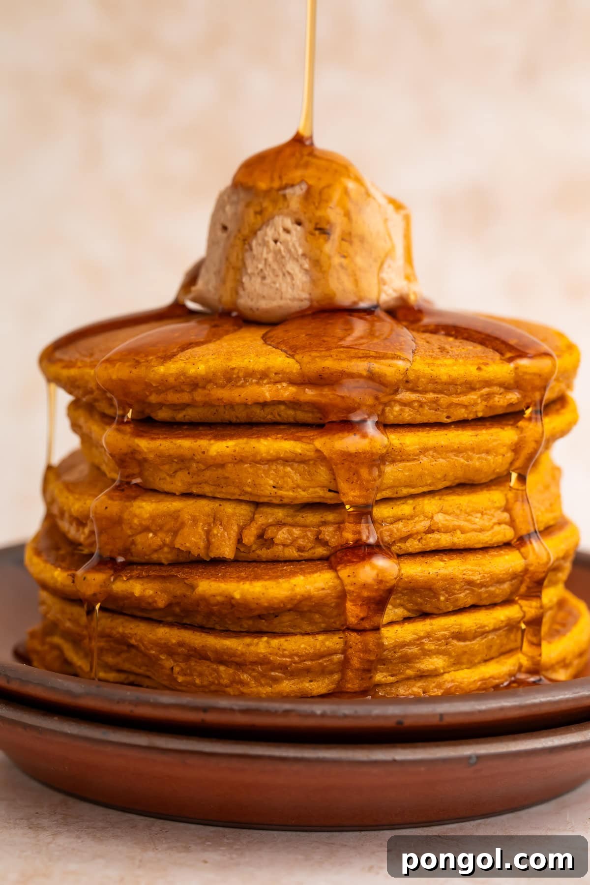 Stack of golden pumpkin protein pancakes with cinnamon butter and maple syrup drizzling down