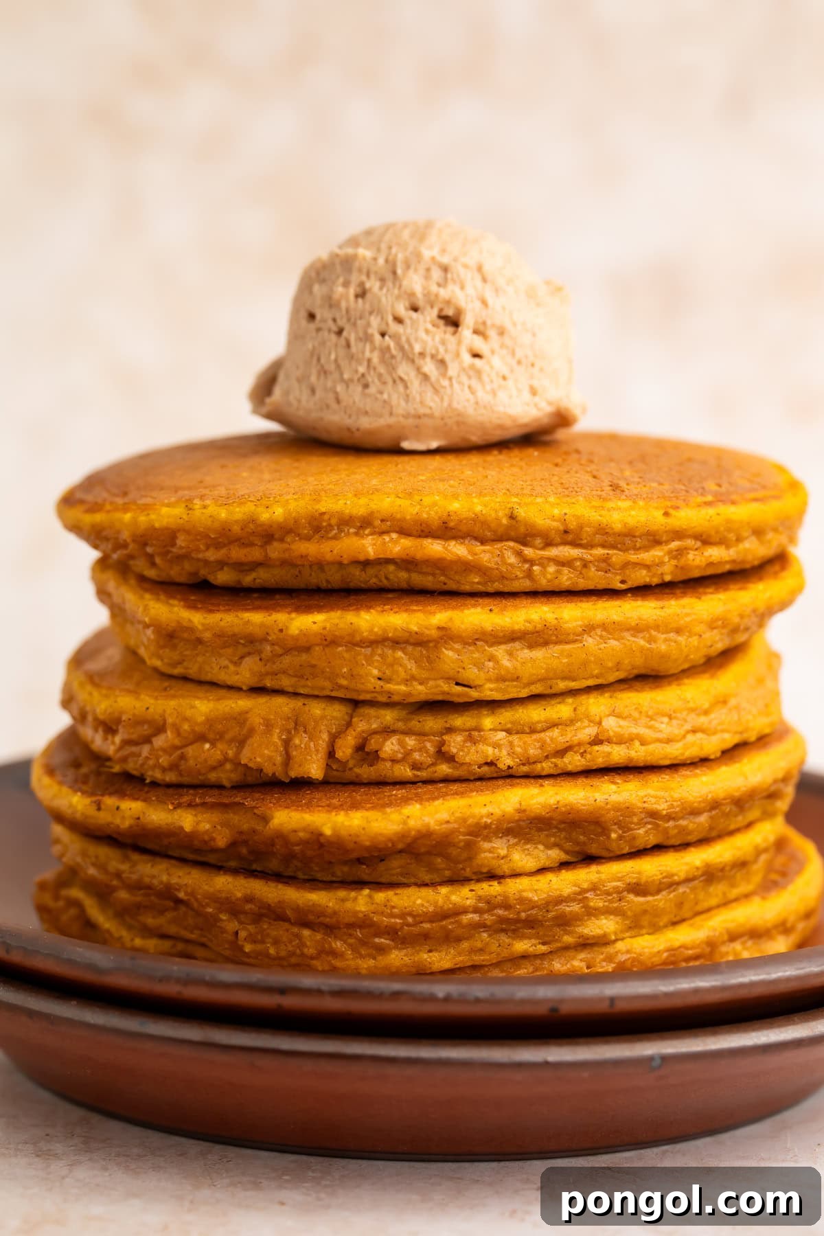 Clean stack of golden pumpkin protein pancakes with single cinnamon butter scoop on top