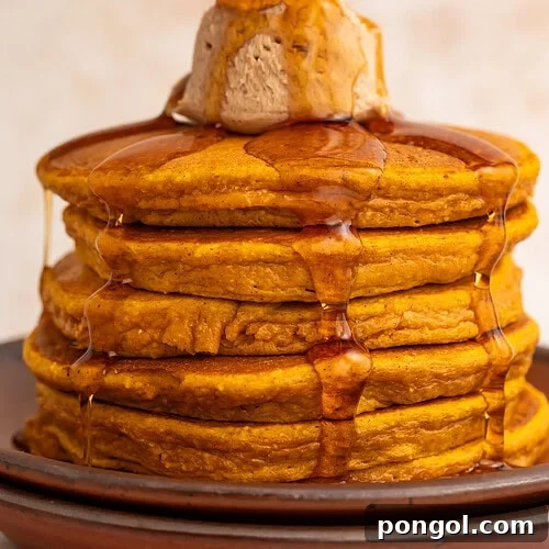 Stack of golden pumpkin protein pancakes with cinnamon butter and maple syrup drizzling down