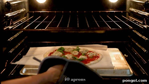 Gently sliding paleo pizza on parchment onto a preheated overturned baking sheet in the oven