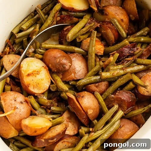 White slow cooker filled with cooked swamp potatoes showing tender red potatoes, green beans, and sliced sausage with serving spoon