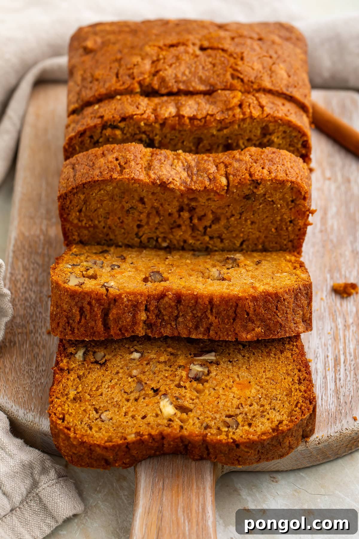 Sliced sweet potato bread with pecans on wooden cutting board showing moist orange crumb