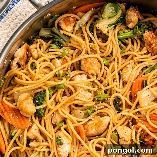A vibrant close-up of sesame garlic chicken lo mein in a large skillet, showcasing a delightful mix of noodles, tender broccoli, crisp carrots, and golden chicken pieces, all beautifully garnished with sesame seeds.