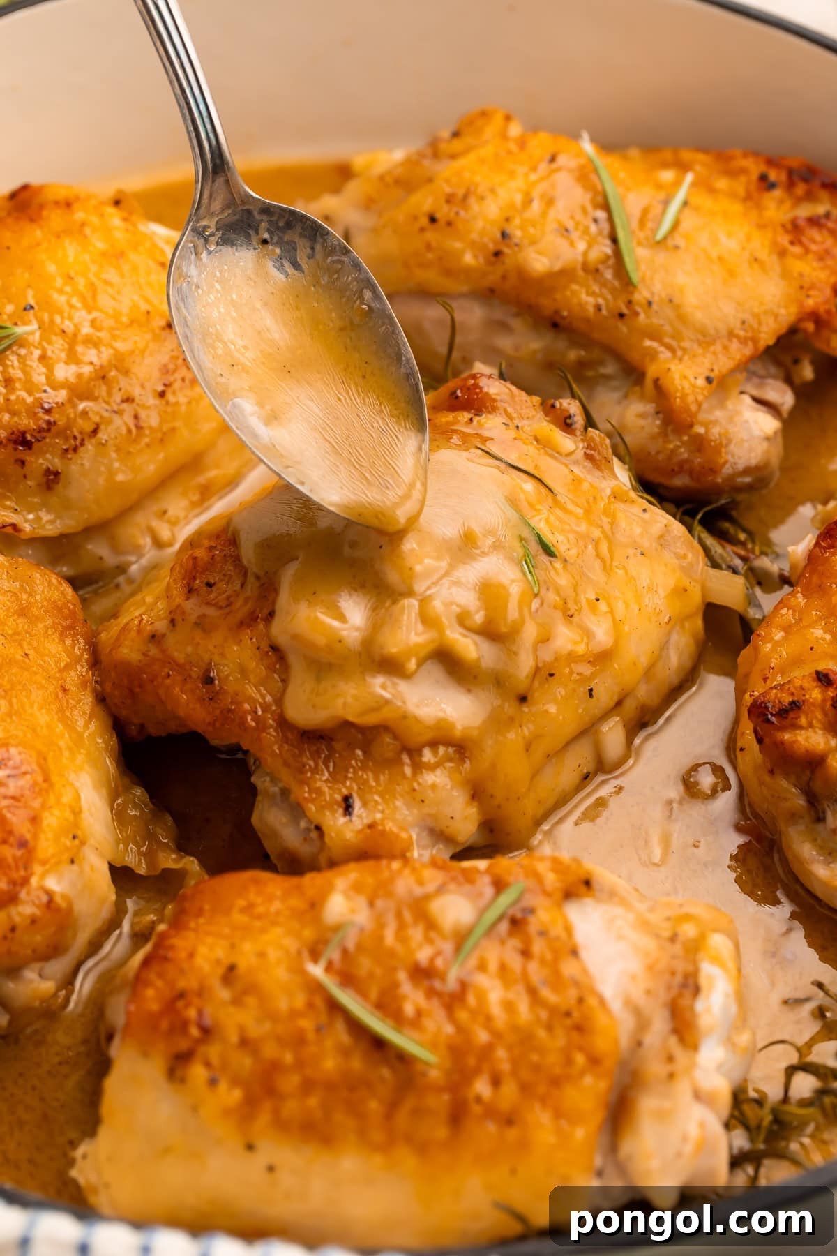 Sticky Maple Dijon Chicken Thighs 3 A spoon expertly drizzling glossy maple dijon sauce over crispy chicken thighs with fresh rosemary garnish.