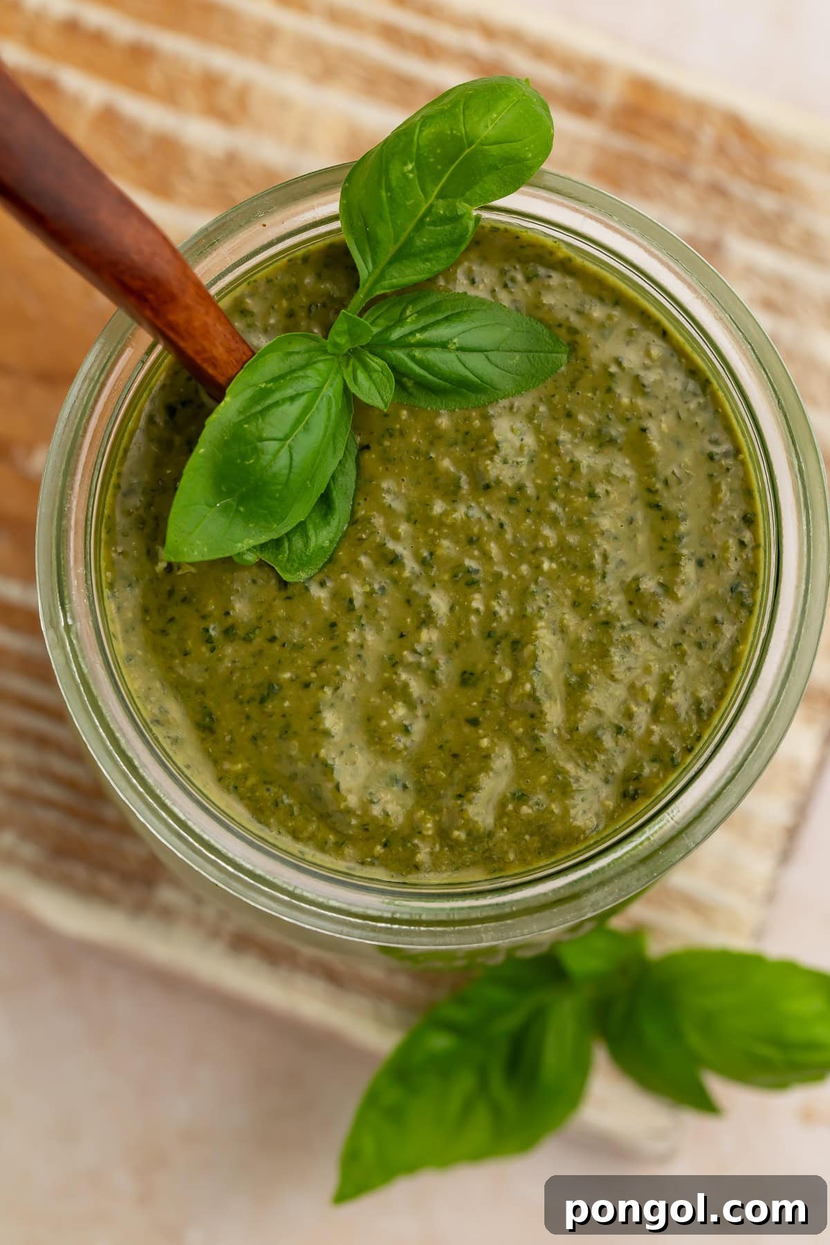 Creamy pesto sauce in a glass jar with fresh basil leaves and wooden spoon