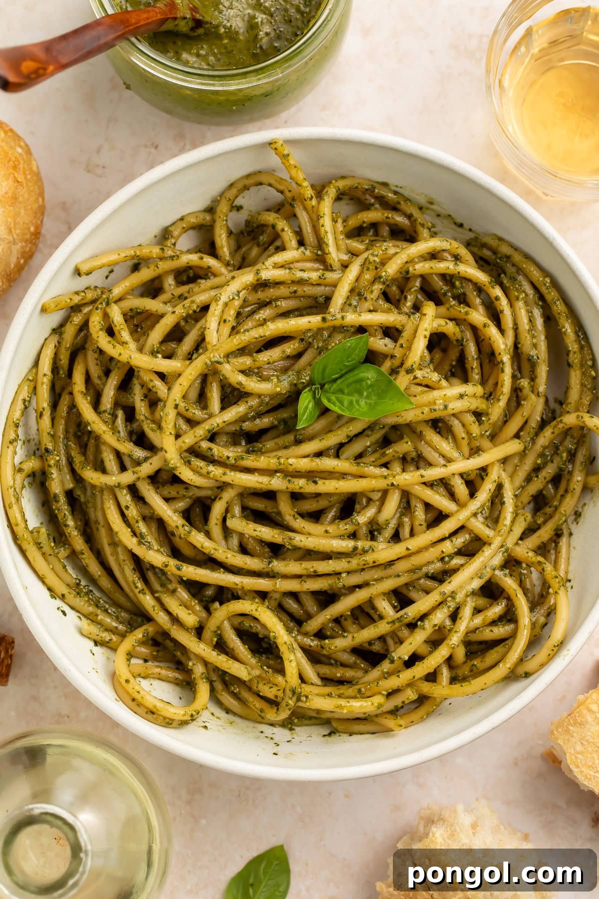 Spaghetti tossed with creamy pesto sauce in white bowl with basil garnish