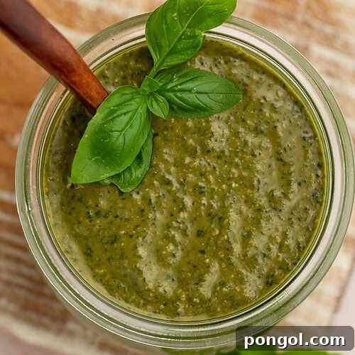 Creamy pesto sauce in a glass jar with fresh basil leaves and wooden spoon