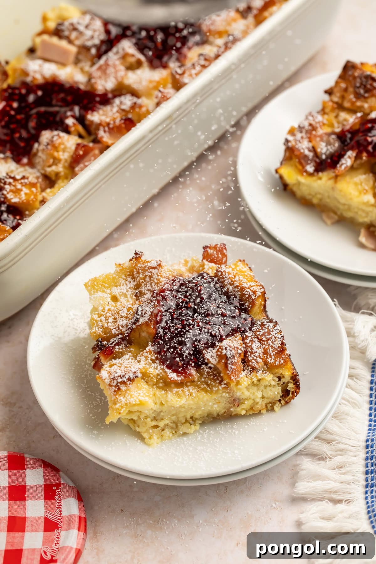 Monte Cristo casserole slices on white plates with raspberry jam and powdered sugar.
