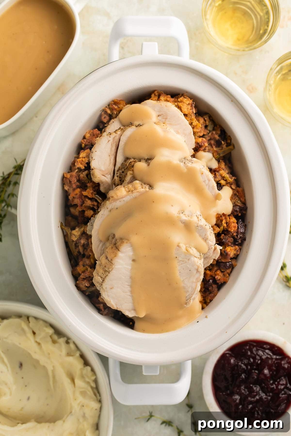 Overhead view of thick slices of turkey, smothered in gravy, on top of cooked stuffing and green beans in a Crockpot.