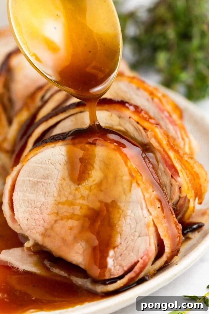 bacon wrapped pork tenderloin on a plate with brown sugar glaze being spooned over the top