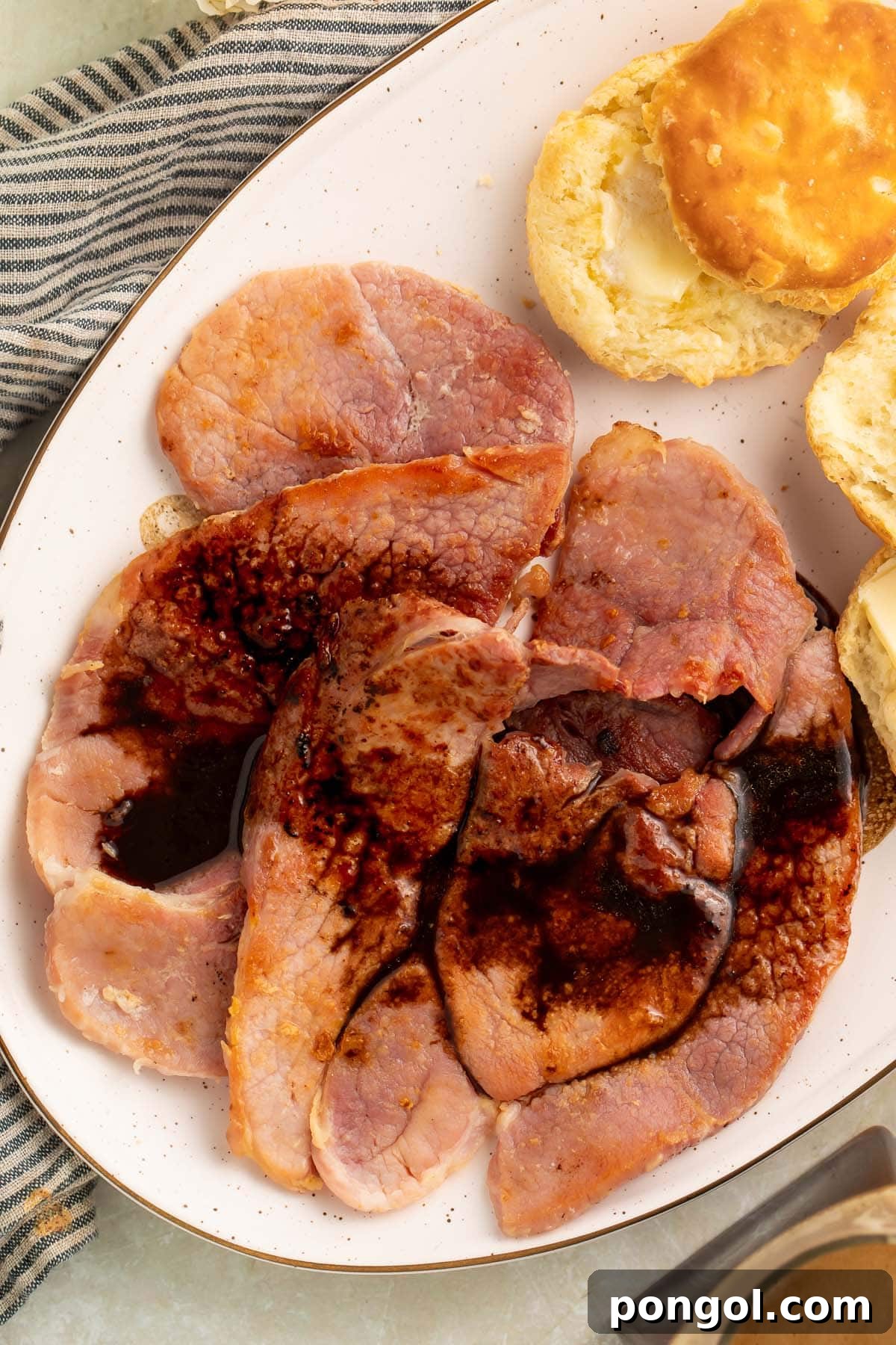 Red eye gravy poured over country ham on an oval platter with fluffy biscuits.