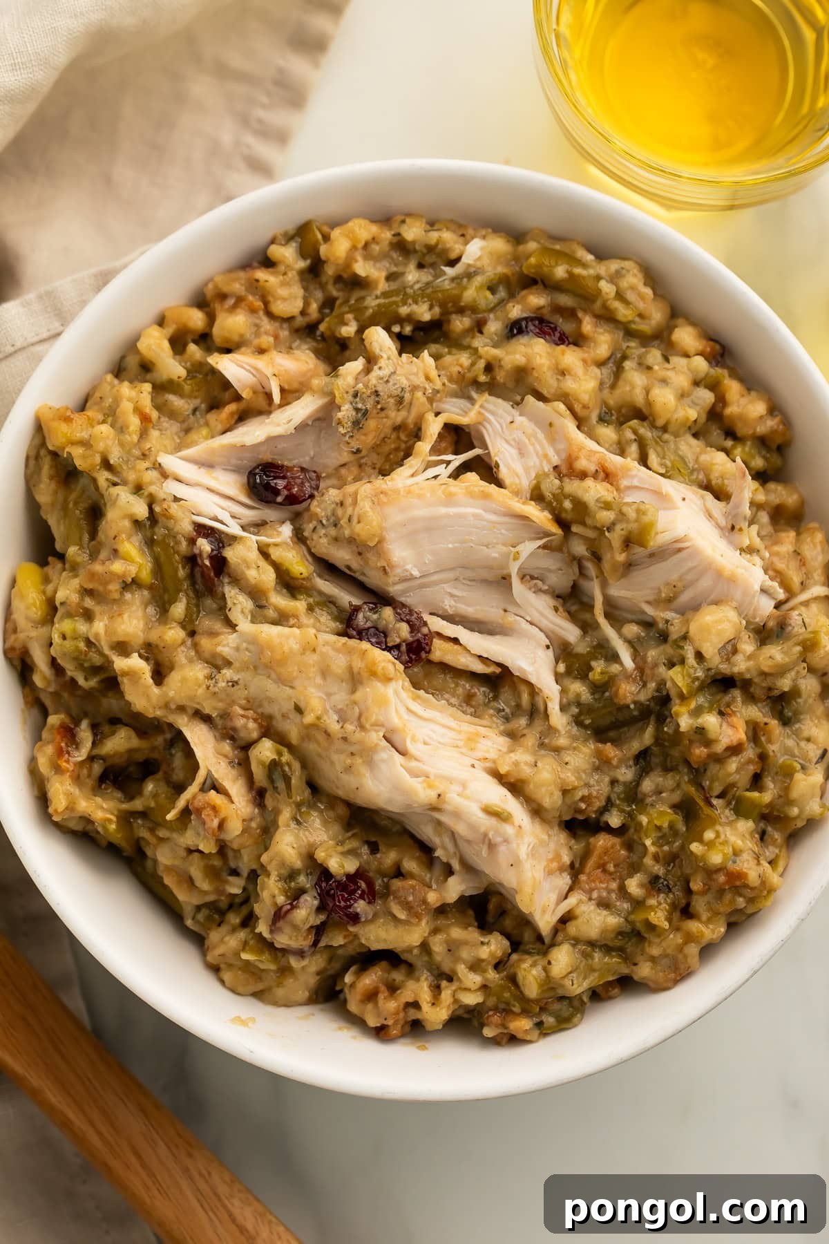 White bowl filled with shredded chicken and herb stuffing with green beans and dried cranberries on wooden table