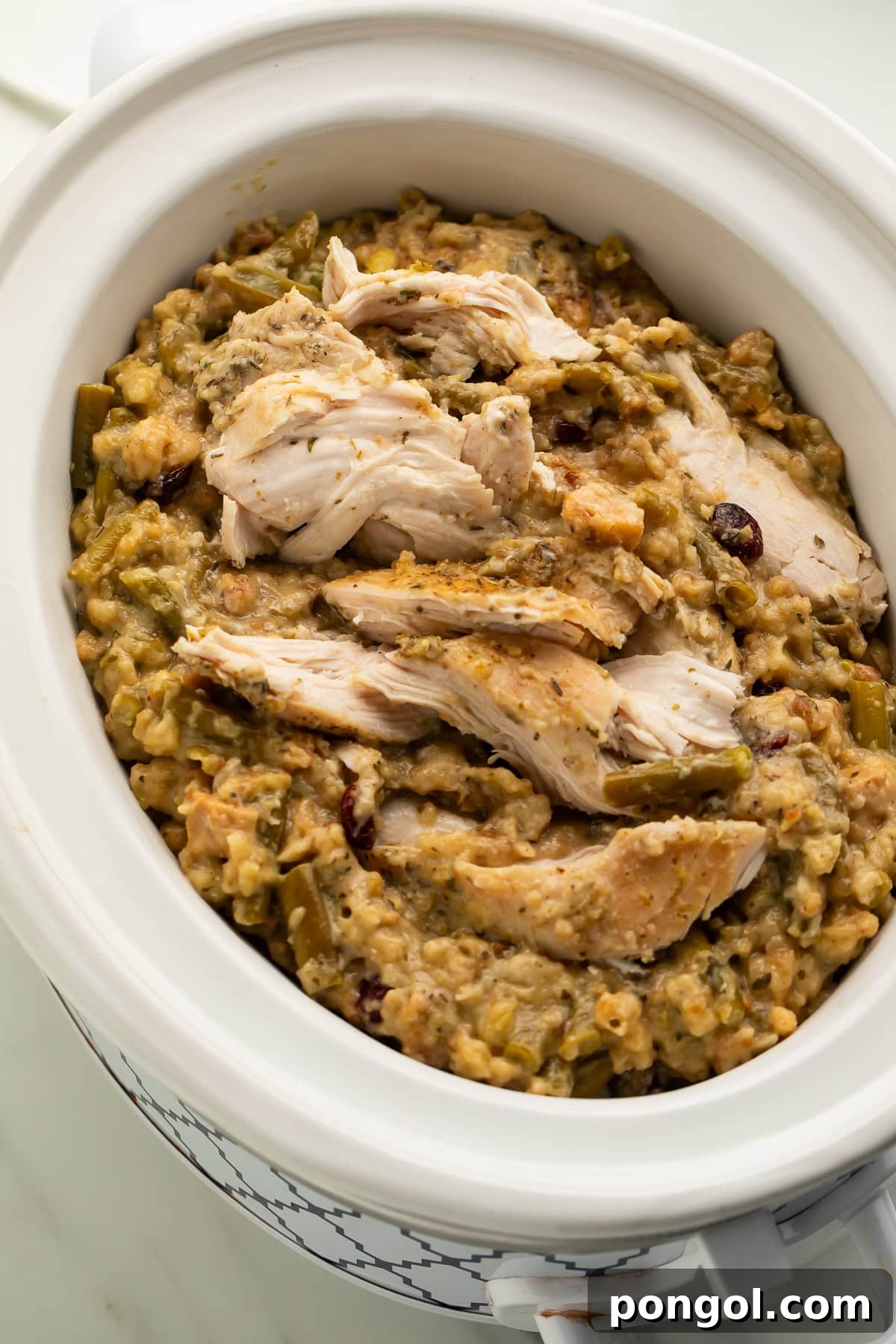 Sliced chicken breasts on top of herb stuffing with green beans and cranberries in white crockpot insert