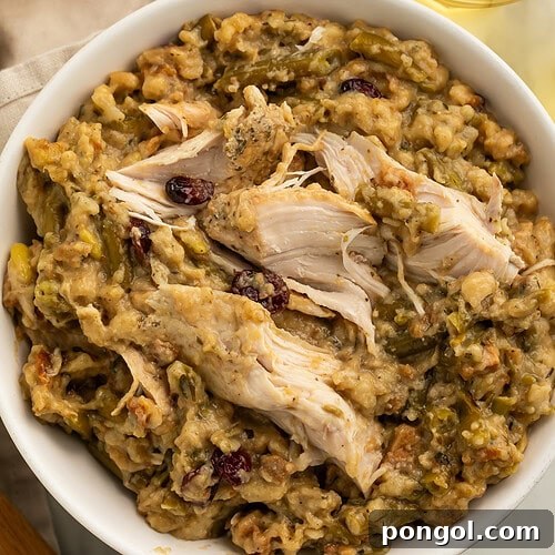 White bowl filled with shredded chicken and herb stuffing with green beans and dried cranberries on wooden table