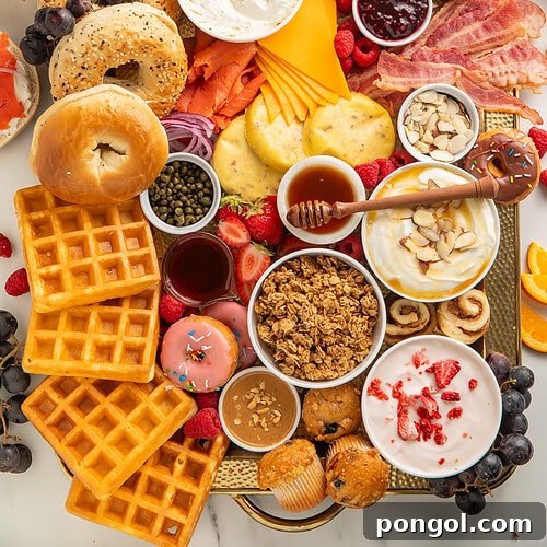 Full breakfast charcuterie board on a wooden tray with bagels, croissants, waffles, yogurt, bacon, cheese, fruit, muffins, and donuts.