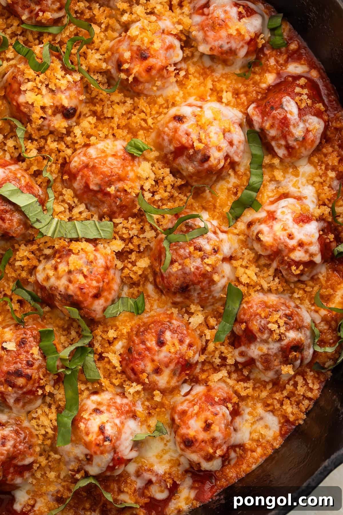 Overhead view of chicken parmesan meatballs in cast iron skillet with melted mozzarella, golden breadcrumbs, and fresh basil.