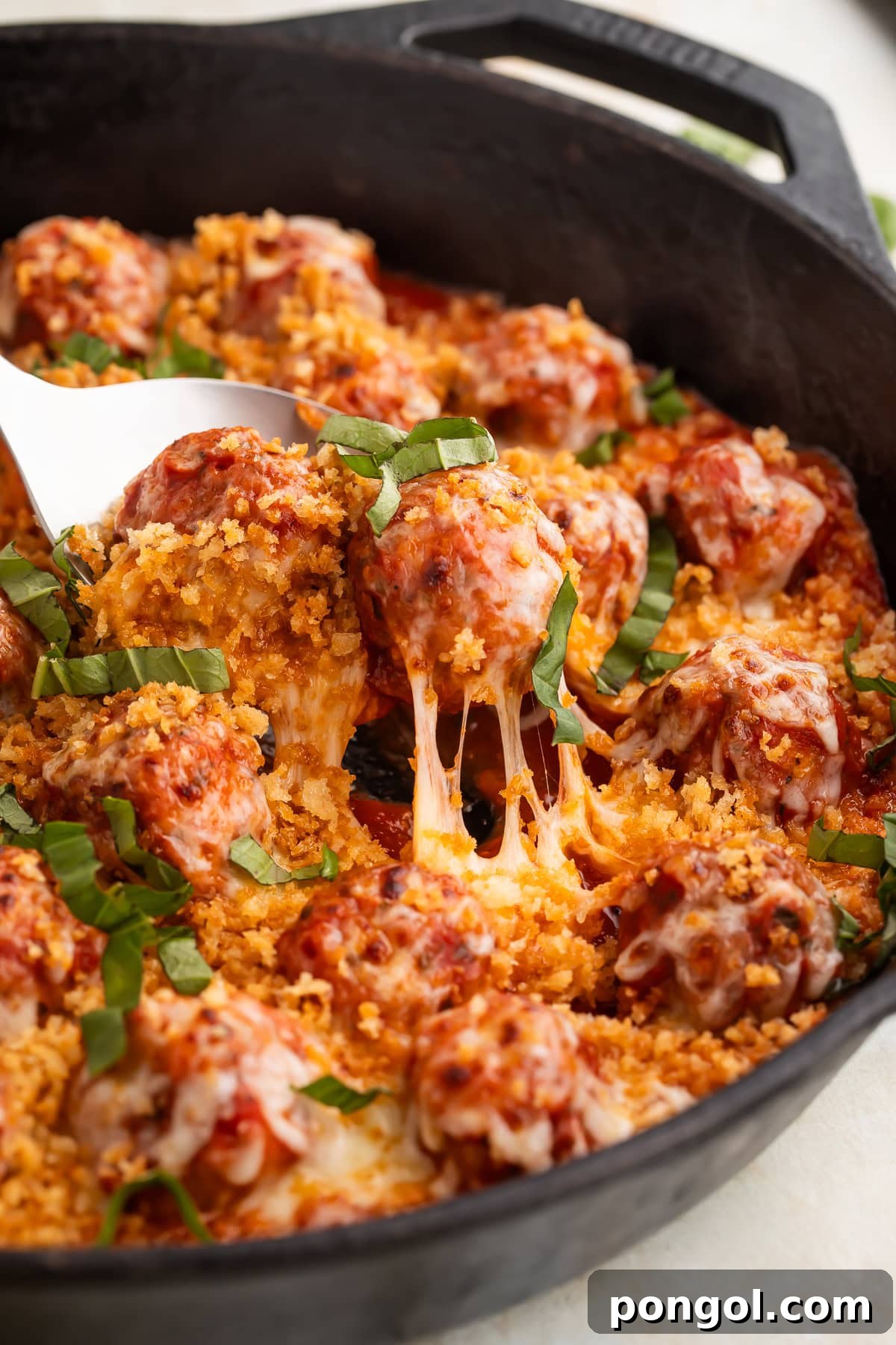 Chicken parmesan meatball being lifted from cast iron skillet with melted mozzarella cheese stretching from the pan.