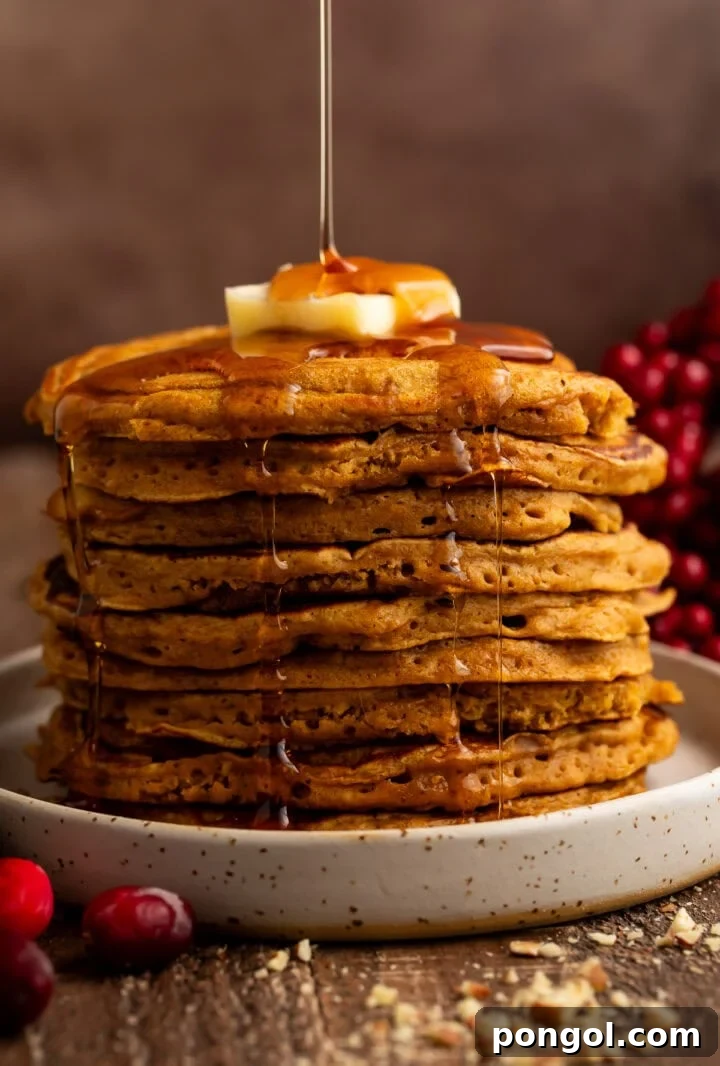 Tall stack of golden gingerbread pancakes with maple syrup being drizzled from above with butter on top