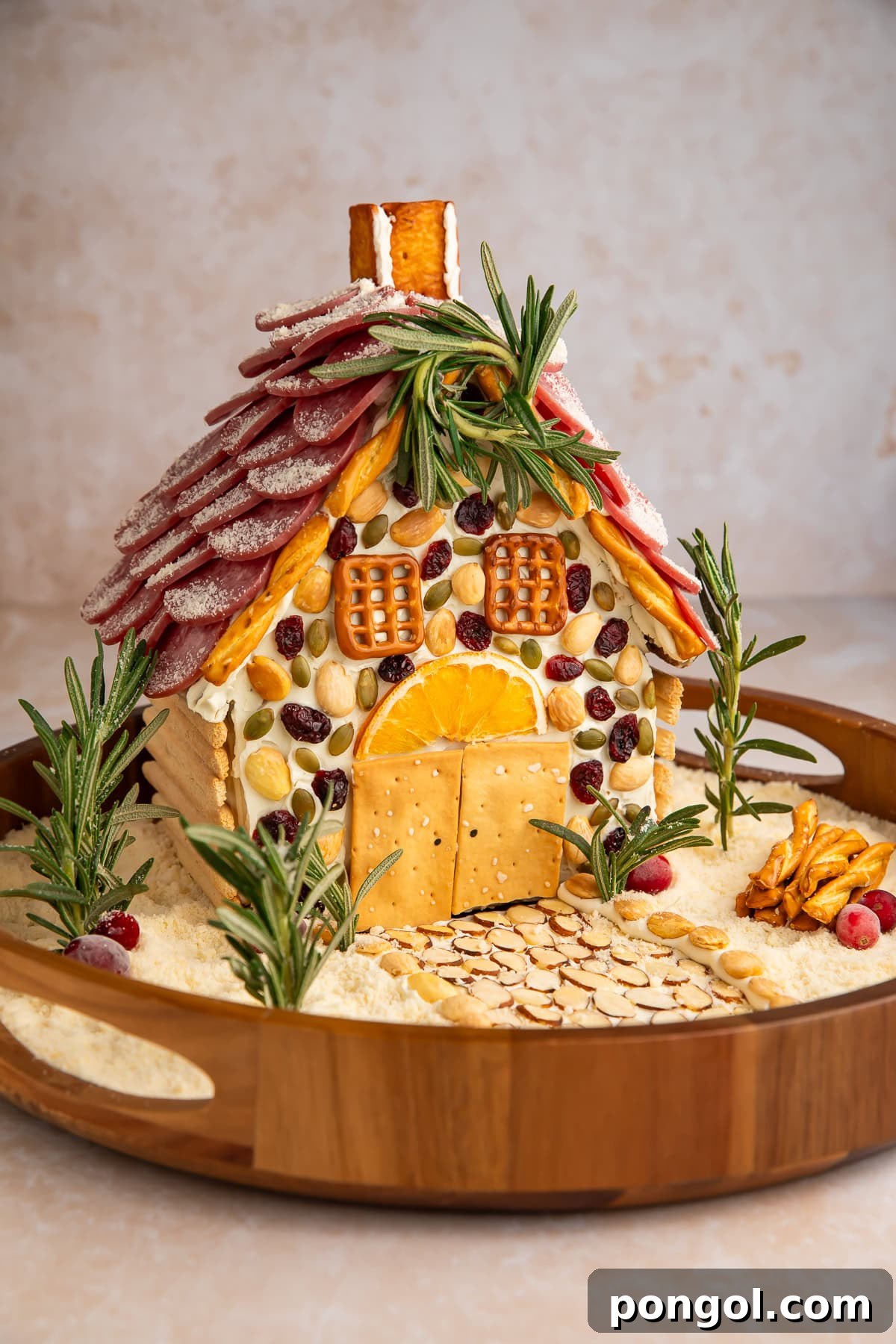 Savory charcuterie chalet with salami shingle roof, pretzel chimney, nuts, and parmesan cheese snow on wooden serving board.