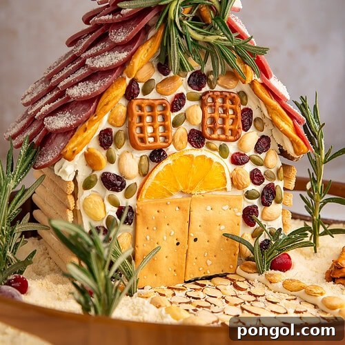 Detailed view of charcuterie chalet with cream cheese mortar, crackers as windows, and rosemary tree garnishes.