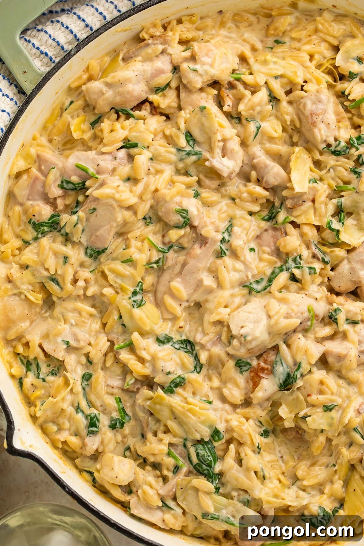 One Pan Creamy Spinach Artichoke Chicken Orzo 2 Creamy orzo pasta with chicken, spinach, and artichoke hearts in white skillet with melted Parmesan cheese, garnished with fresh herbs