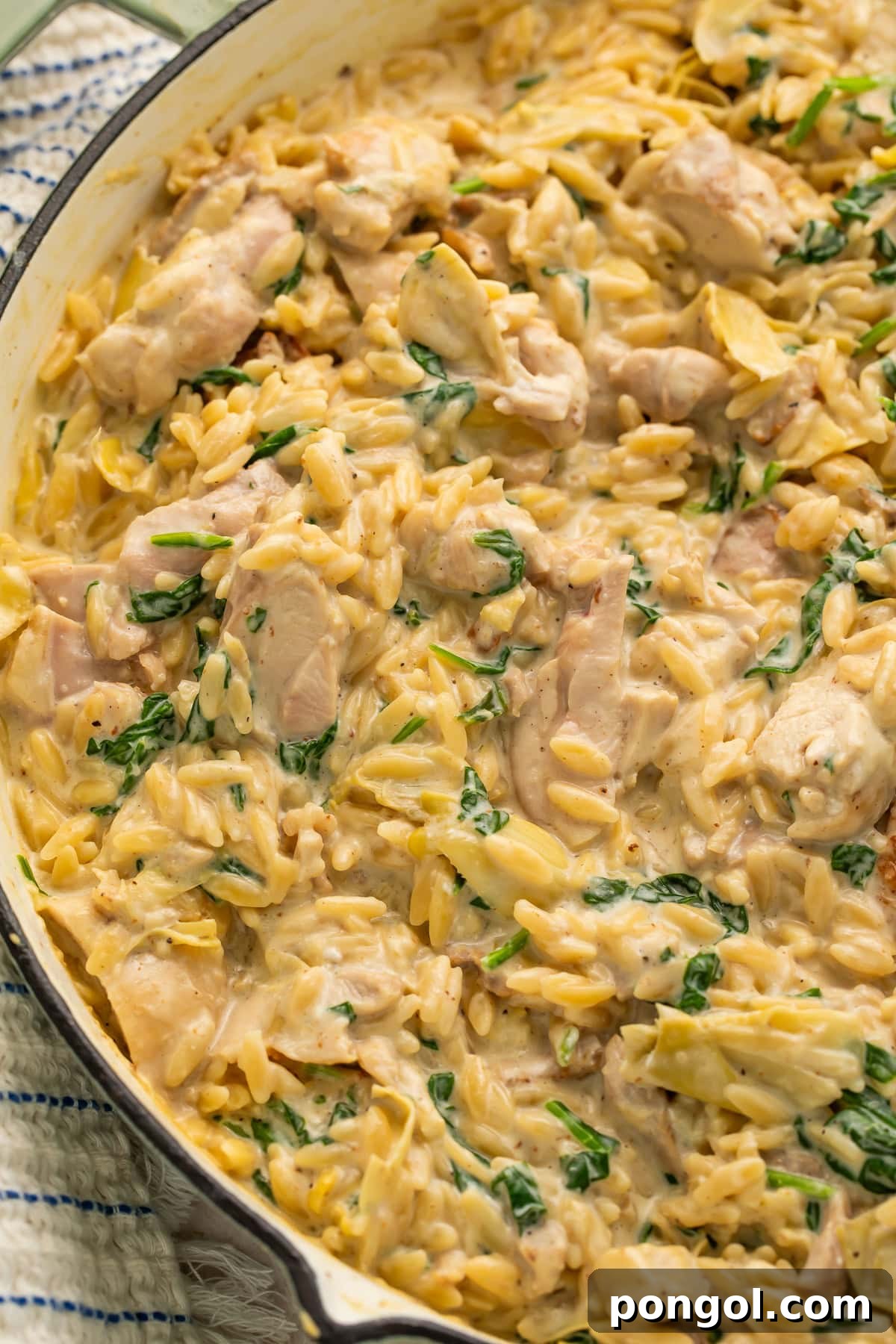 One Pan Creamy Spinach Artichoke Chicken Orzo 4 Overhead view of creamy chicken orzo with spinach, artichokes, and parmesan in white enameled skillet
