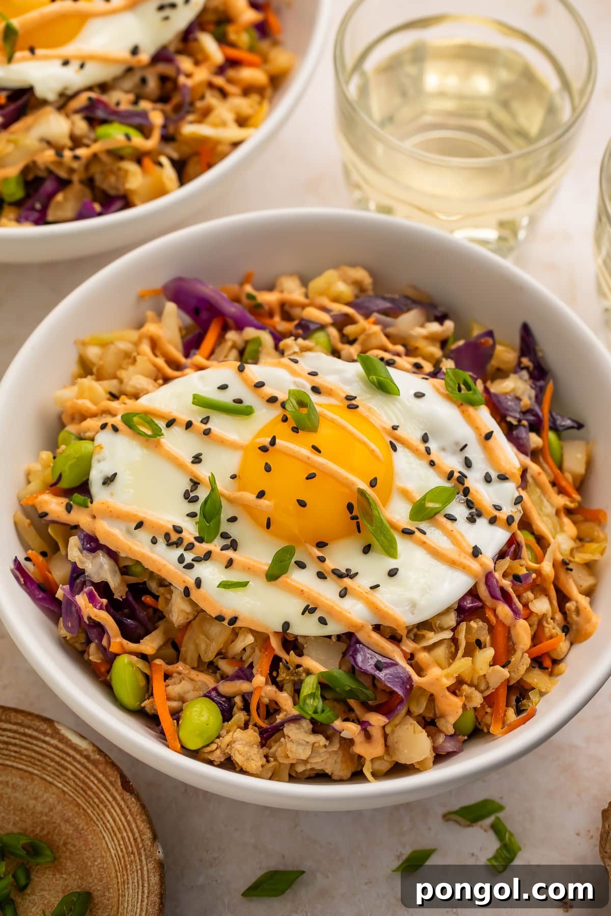High protein egg roll in a bowl topped with a fried egg and drizzled with creamy chili sauce