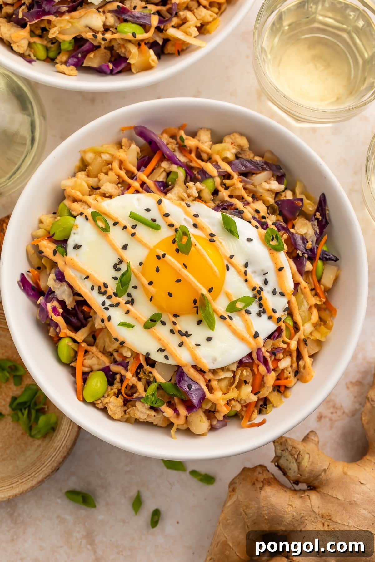 Close-up of egg roll in a bowl showing ground pork, purple cabbage, edamame, and fried egg with creamy sauce