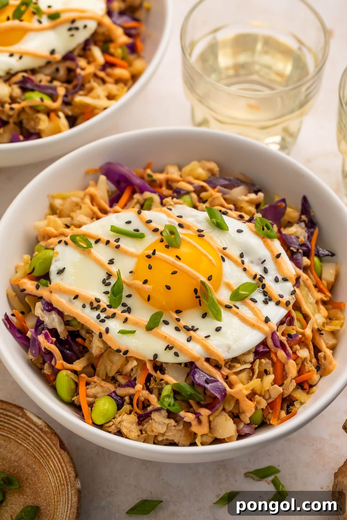 Overhead view of high protein pork egg roll bowl with fried egg, sesame seeds, and green onion garnish