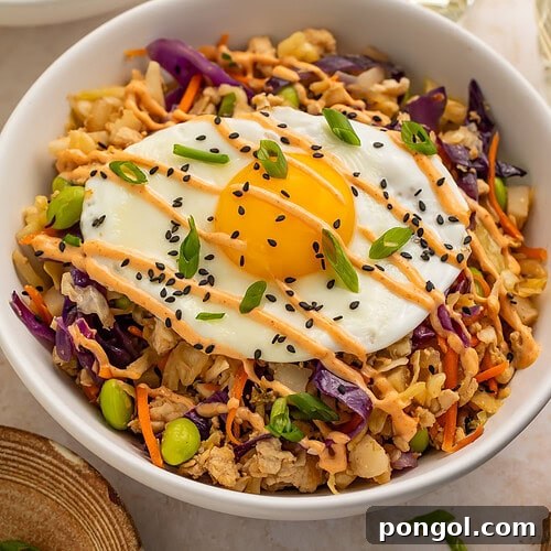 High protein egg roll in a bowl topped with a fried egg and drizzled with creamy chili sauce