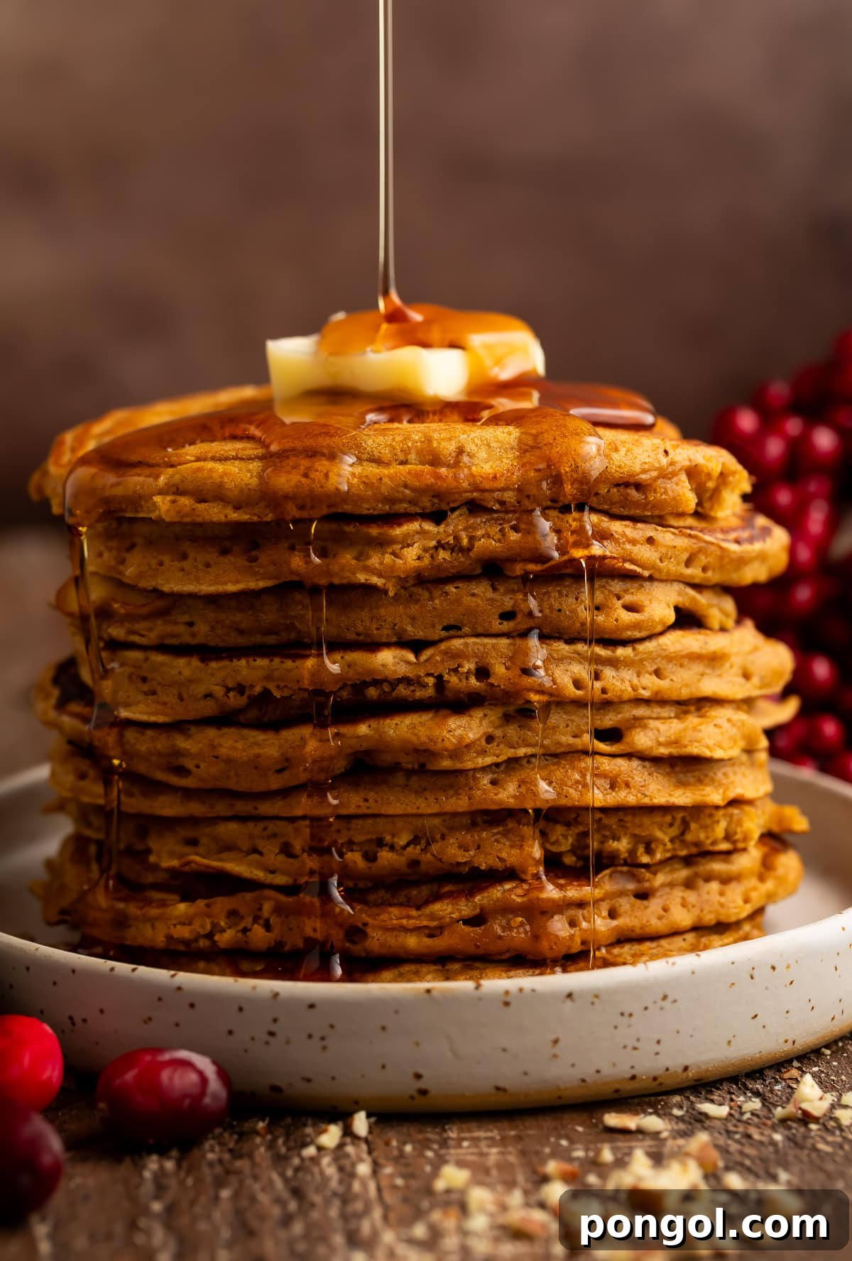 Tall stack of golden gingerbread pancakes with maple syrup being drizzled from above with butter on top